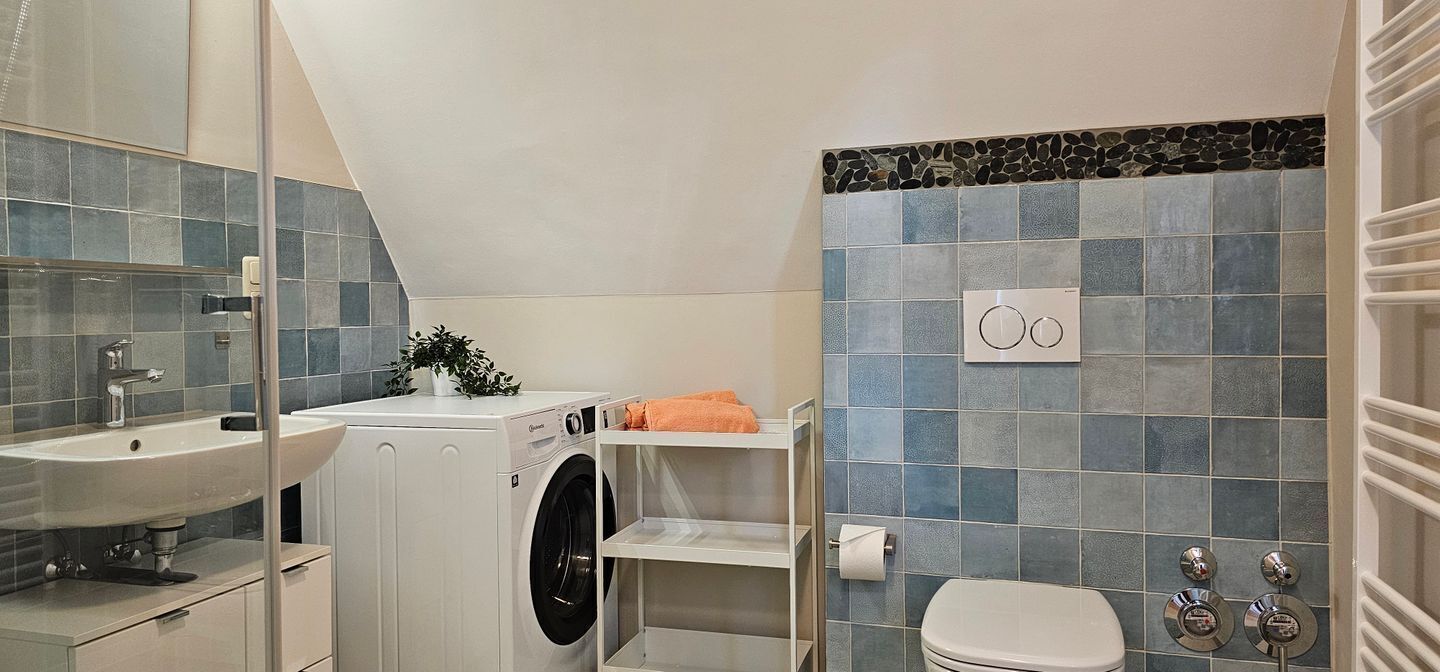Ein kleines Badezimmer mit Waschbecken, Waschmaschine, Toilette und Handtuchhalter.