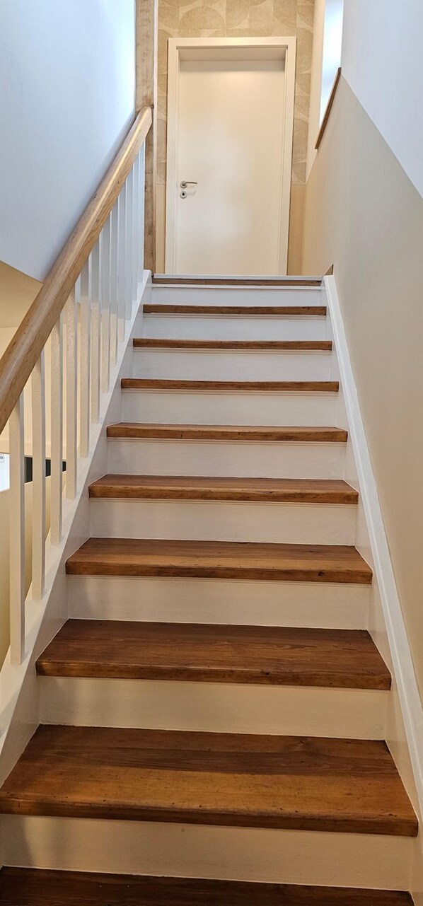 Una escalera con escalones de madera y barandillas blancas que lleva a una puerta.