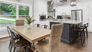 Een moderne keuken met witte kasten, een groot eiland, roestvrijstalen apparatuur en een eethoek met een houten tafel en stoelen.
