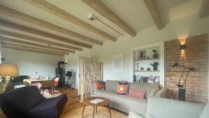 A cozy living room with a fireplace, wooden beams, a sofa, a chair, and a bookshelf. - Newly renovated vacation home - 4 min. to the beach - large, quiet lot surrounded by nature  (Schashagen)