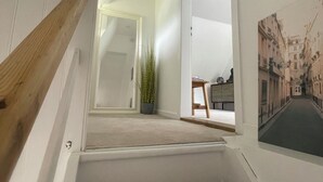 A staircase with a wooden handrail leading to a landing. A potted plant is on the landing, and a framed picture hangs on the wall. - Newly renovated vacation home - 4 min. to the beach - large, quiet lot surrounded by nature  (Schashagen)
