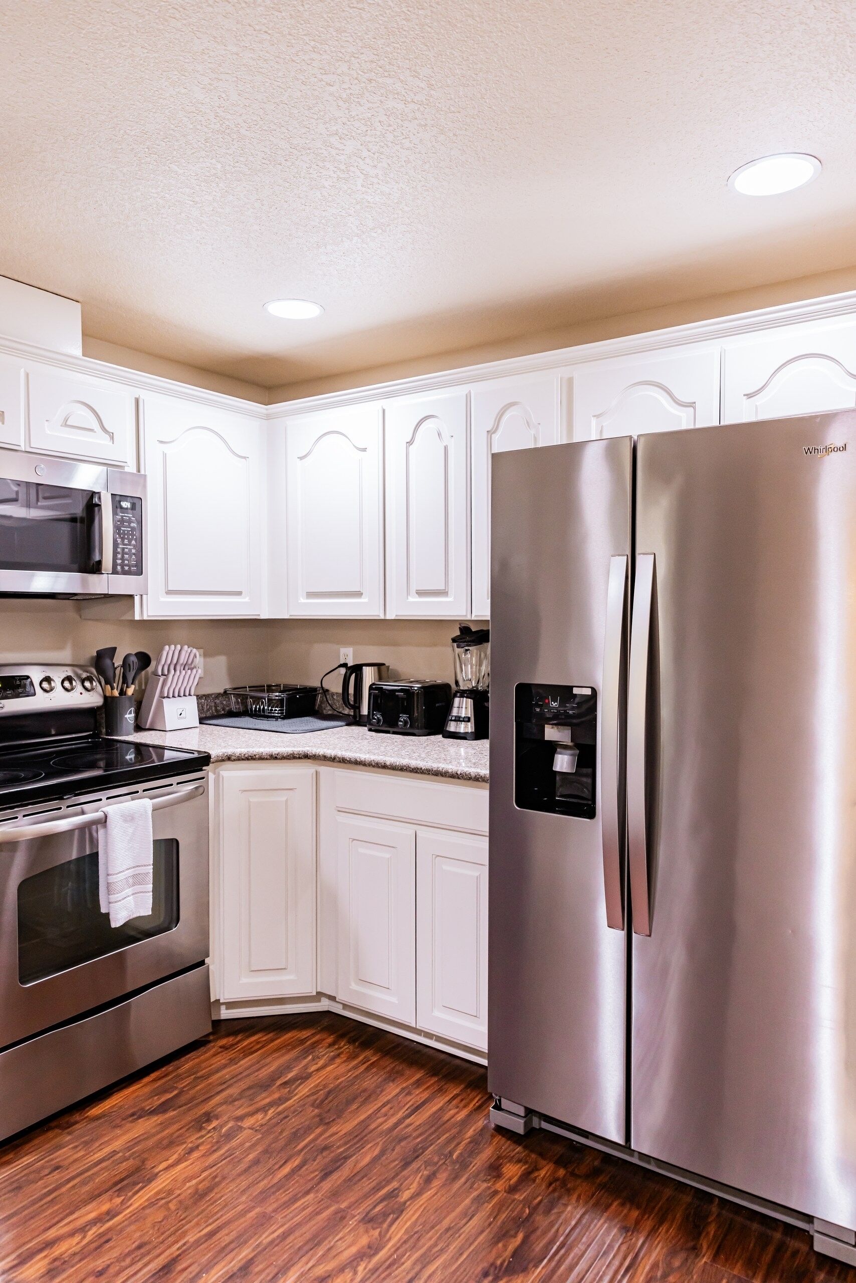 A kitchen with white cabinets, stainless steel appliances, a microwave, a stove, and a refrigerator.