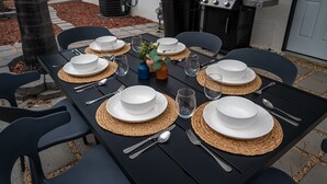 Un área de comedor al aire libre con una mesa negra dispuesta para seis personas, rodeada de sillas negras.