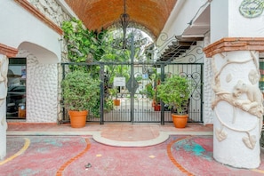 Enter through a beautifully landscaped entrance with a wrought iron gate, flanked by potted plants and a decorative column.