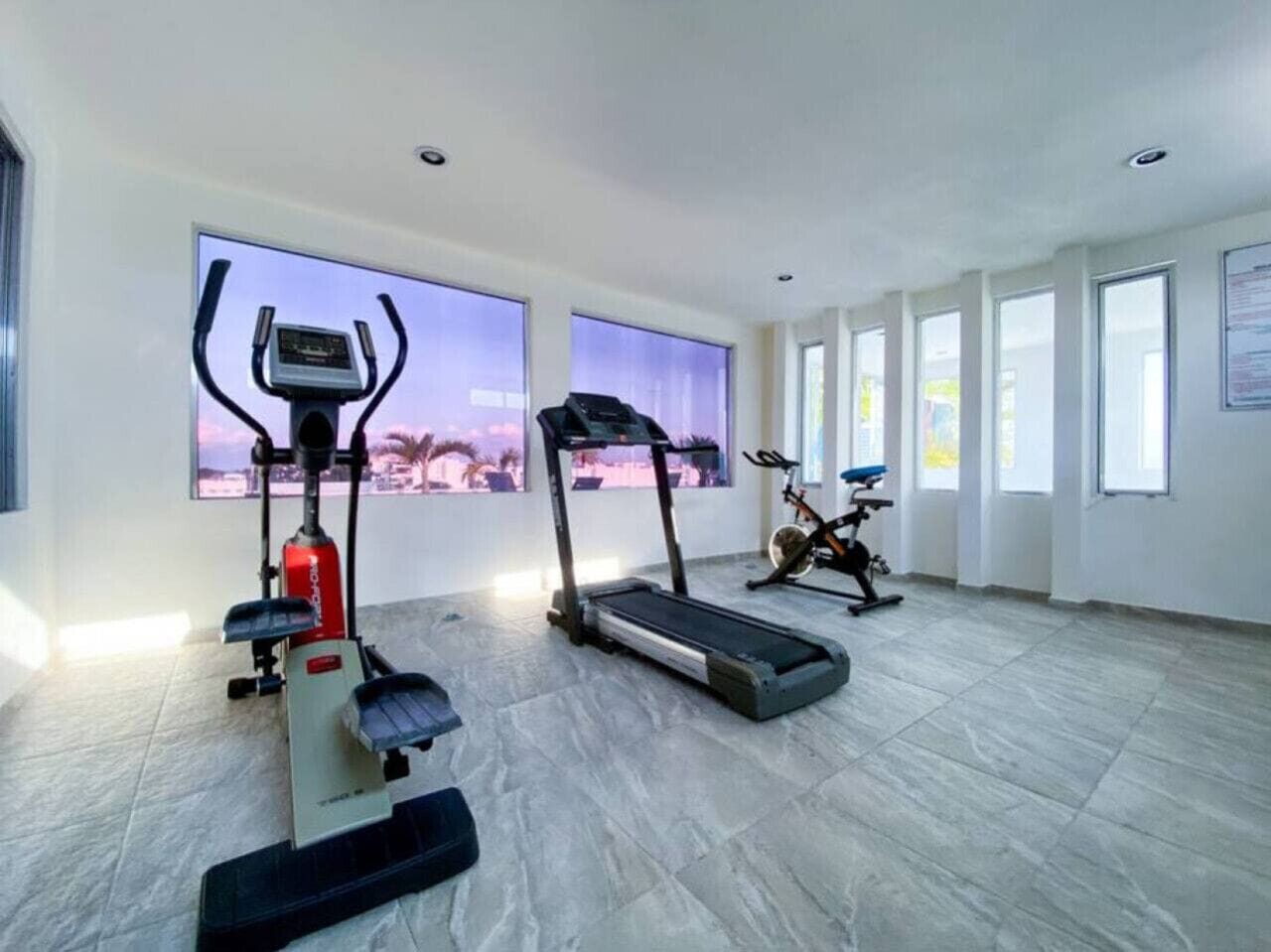 A spacious room with a treadmill, elliptical, and stationary bike, large windows, and a tiled floor.