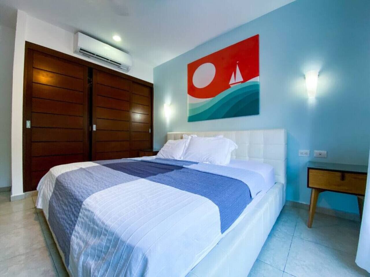 Een slaapkamer met een bed, nachtkastje, wandairconditioning en een deur.