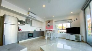 Una cocina moderna con refrigerador, microondas y estufa. Cuenta con un área de comedor con sillas y una mesa. Un televisor de pantalla plana está montado en un mueble.