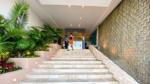 Una escalera conduce a un vestíbulo con una pared de piedra y vegetación a los lados.