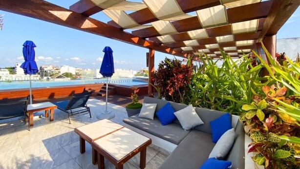Un área de estar cubierta al aire libre con vista a la piscina, un sofá con cojines y una mesa.