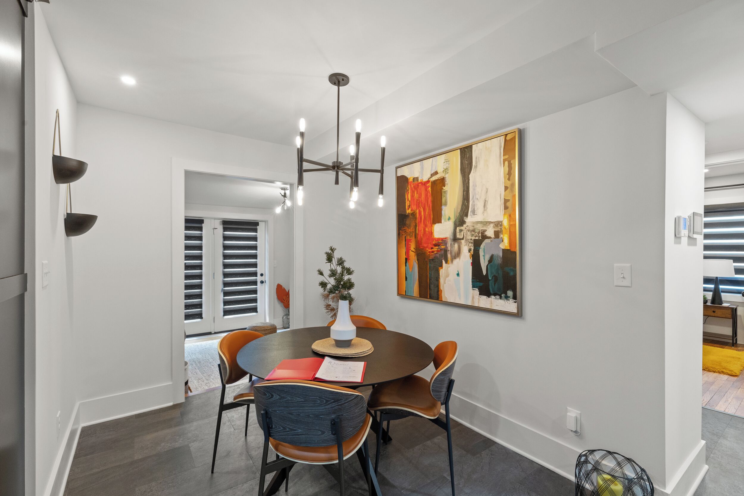 A dining area with a round table, chairs, a chandelier, and a painting on the wall.