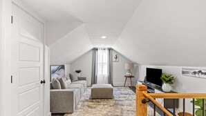 Een modern loft appartement met een grijze bank, een houten trap en een televisie.