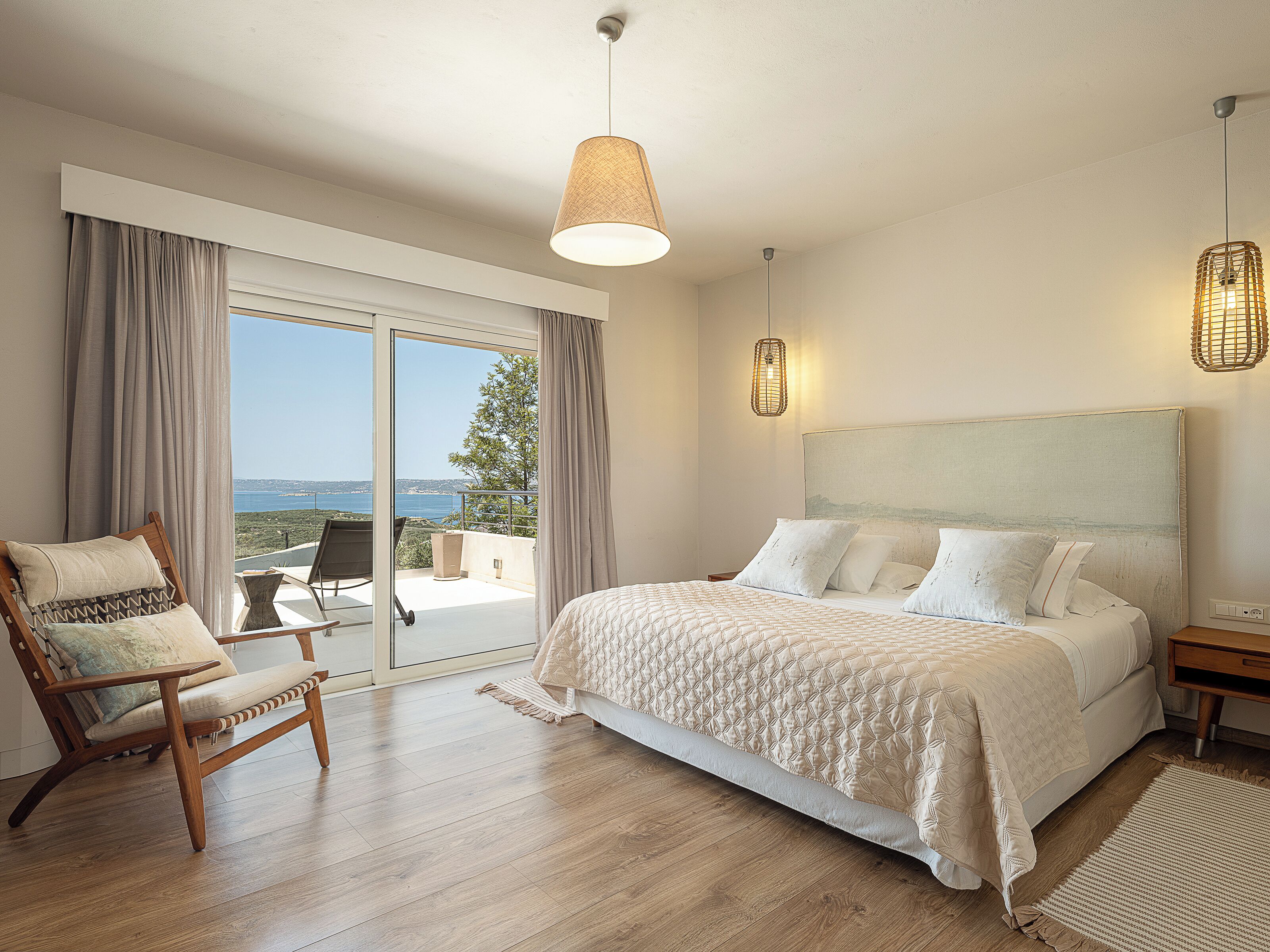 Une chambre avec un grand lit, une chaise, un balcon avec vue et deux lampes suspendues.