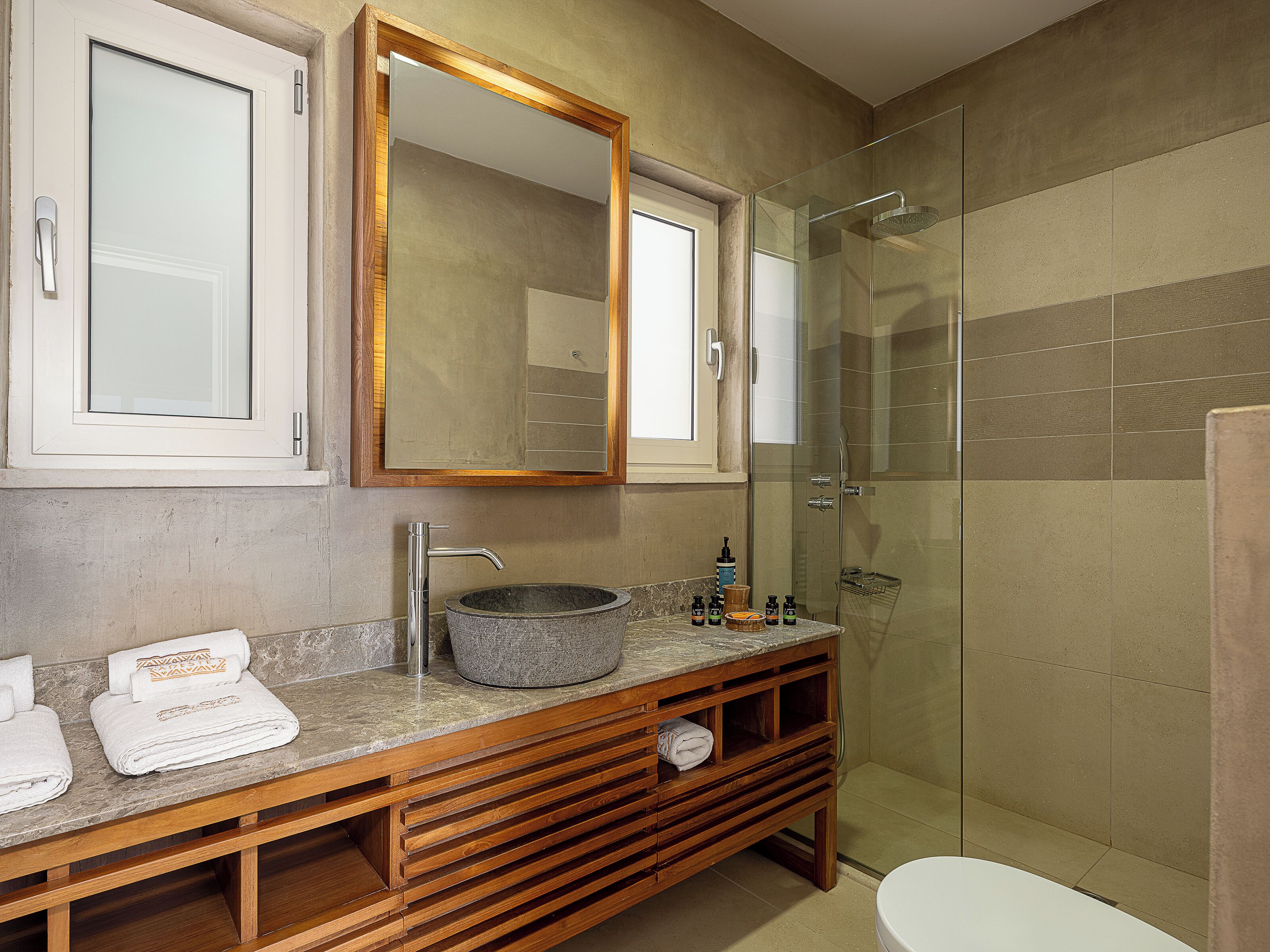 A bathroom with a wooden vanity, a large mirror, a glass-enclosed shower, and a white toilet.