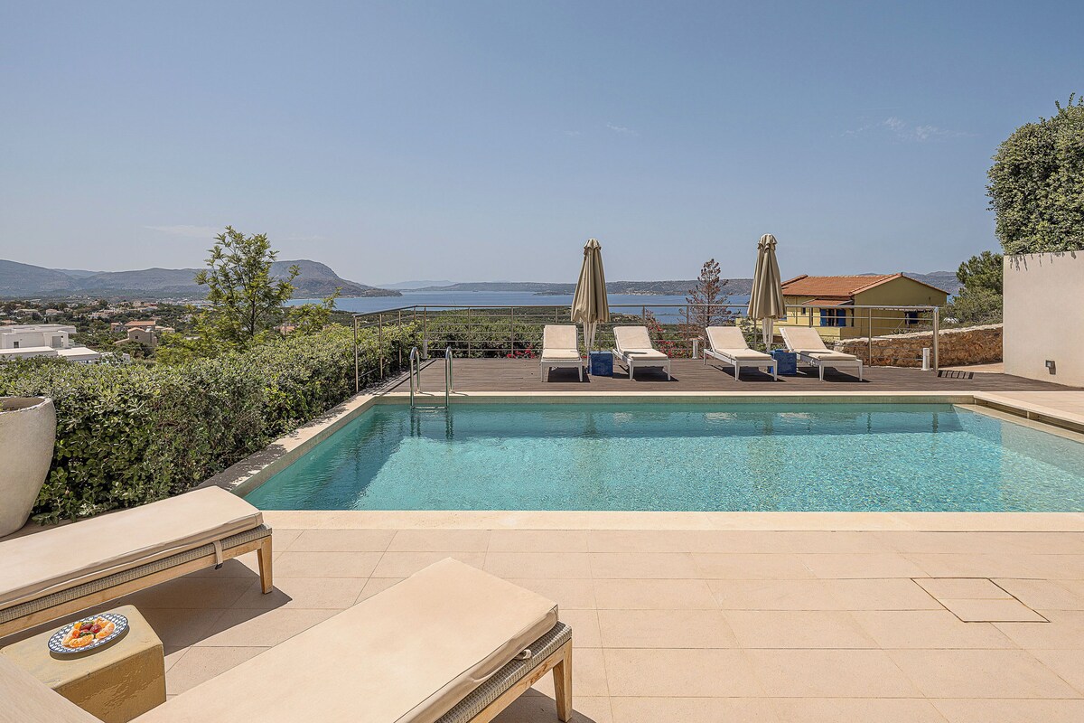 A pool area with lounge chairs and umbrellas, overlooking a scenic landscape with mountains and a body of water.