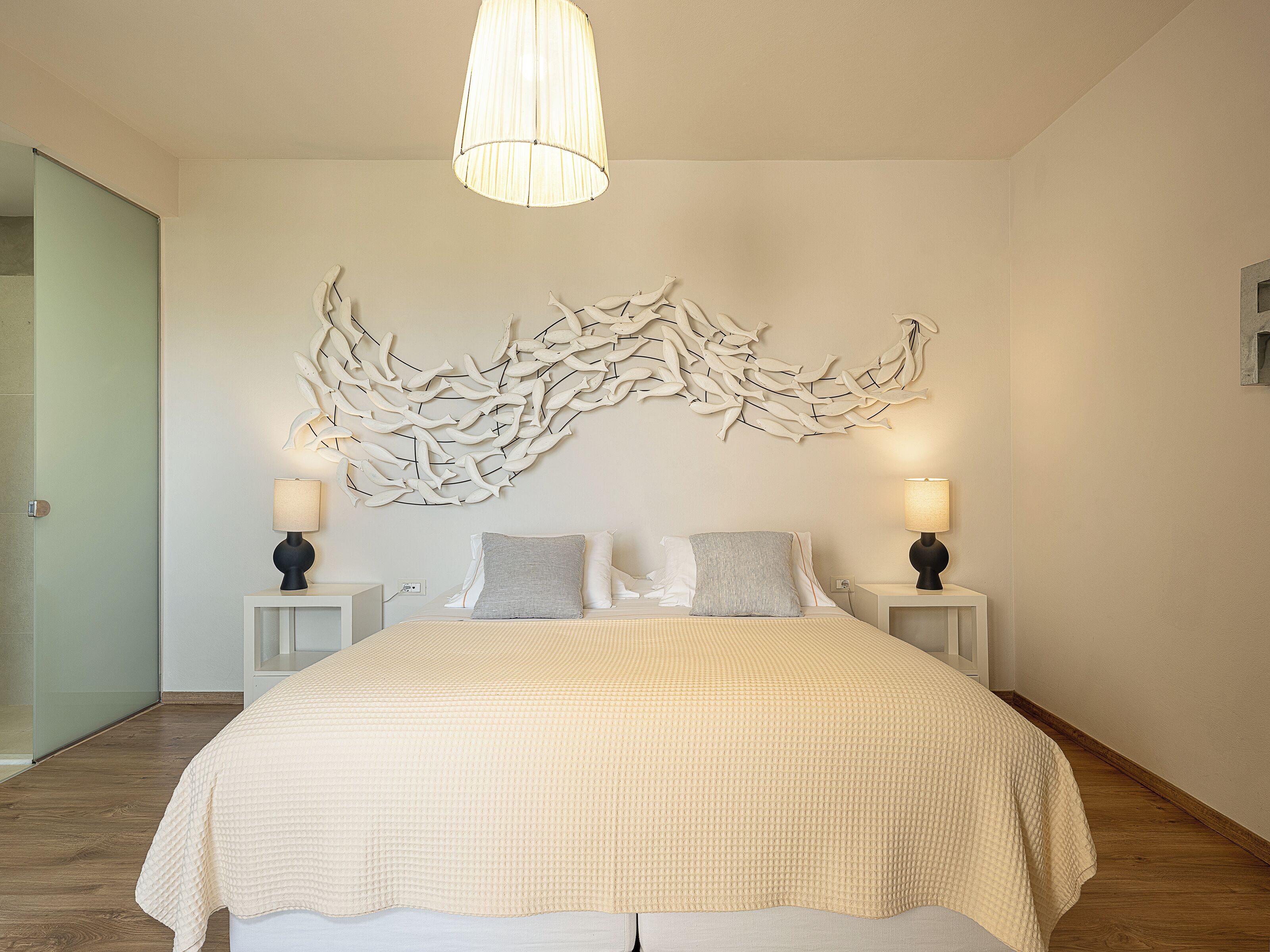 Ein Schlafzimmer mit einem großen Bett, zwei Nachttischlampen, einem Wandbild und Holzboden.