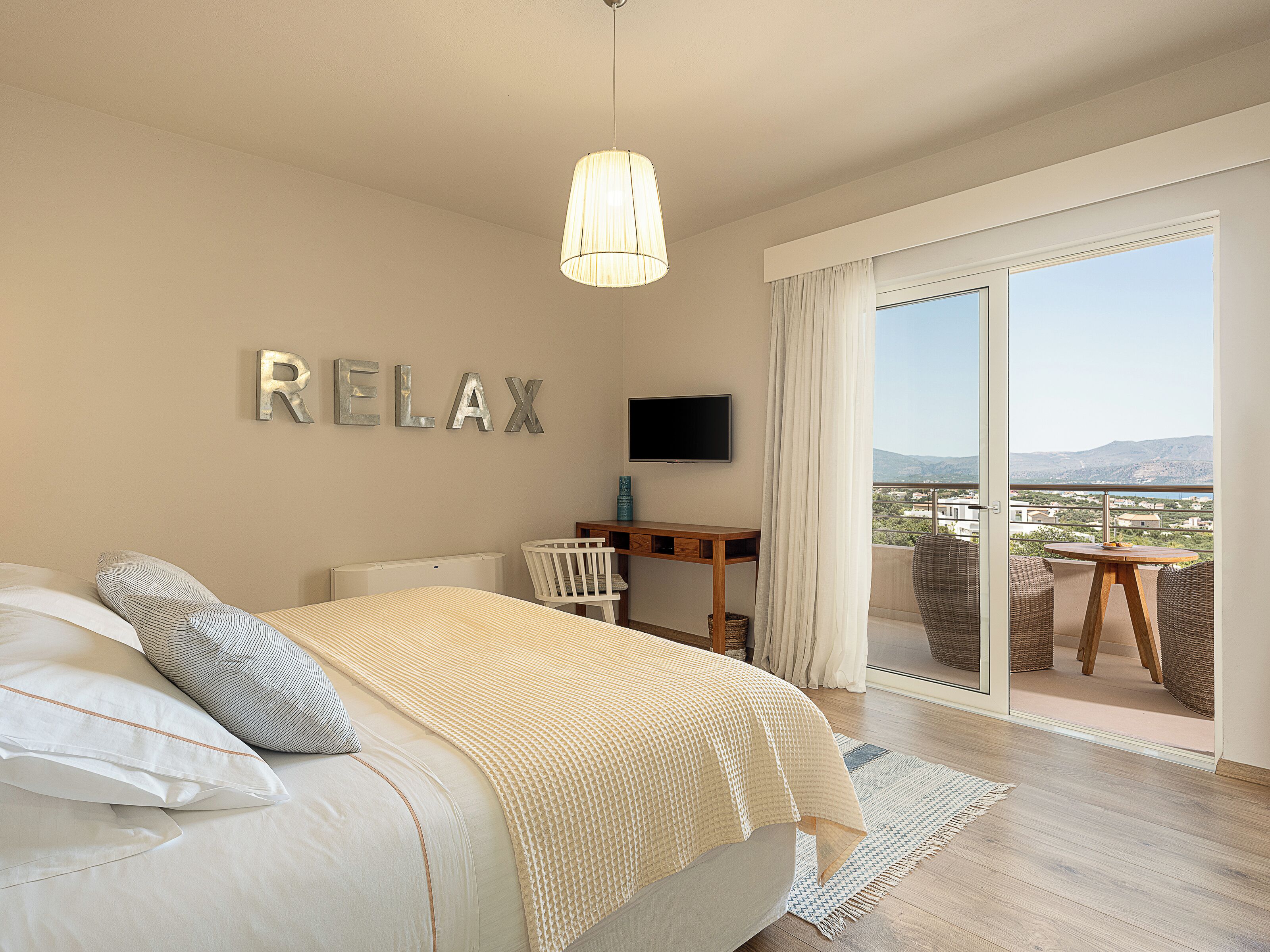 Ein Schlafzimmer mit Bett, Schreibtisch, Fernseher und einem Balkon mit Blick.