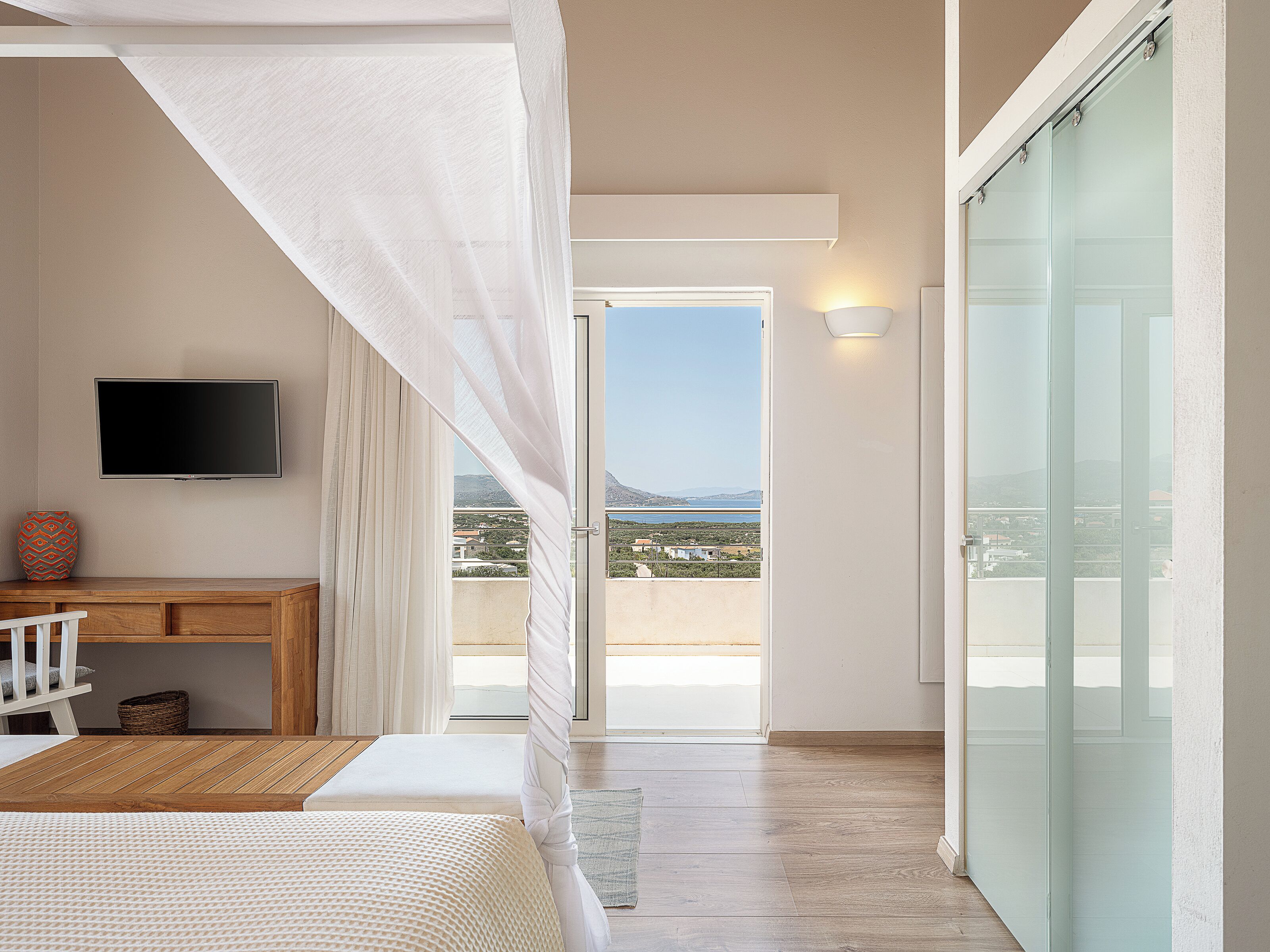 Un dormitorio con cama, escritorio, televisor y balcón con vista al mar.