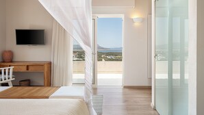 A bedroom with a bed, a desk, a TV, and a balcony with a view of the sea. - Adeste Seaview Villas (Apokoronas)