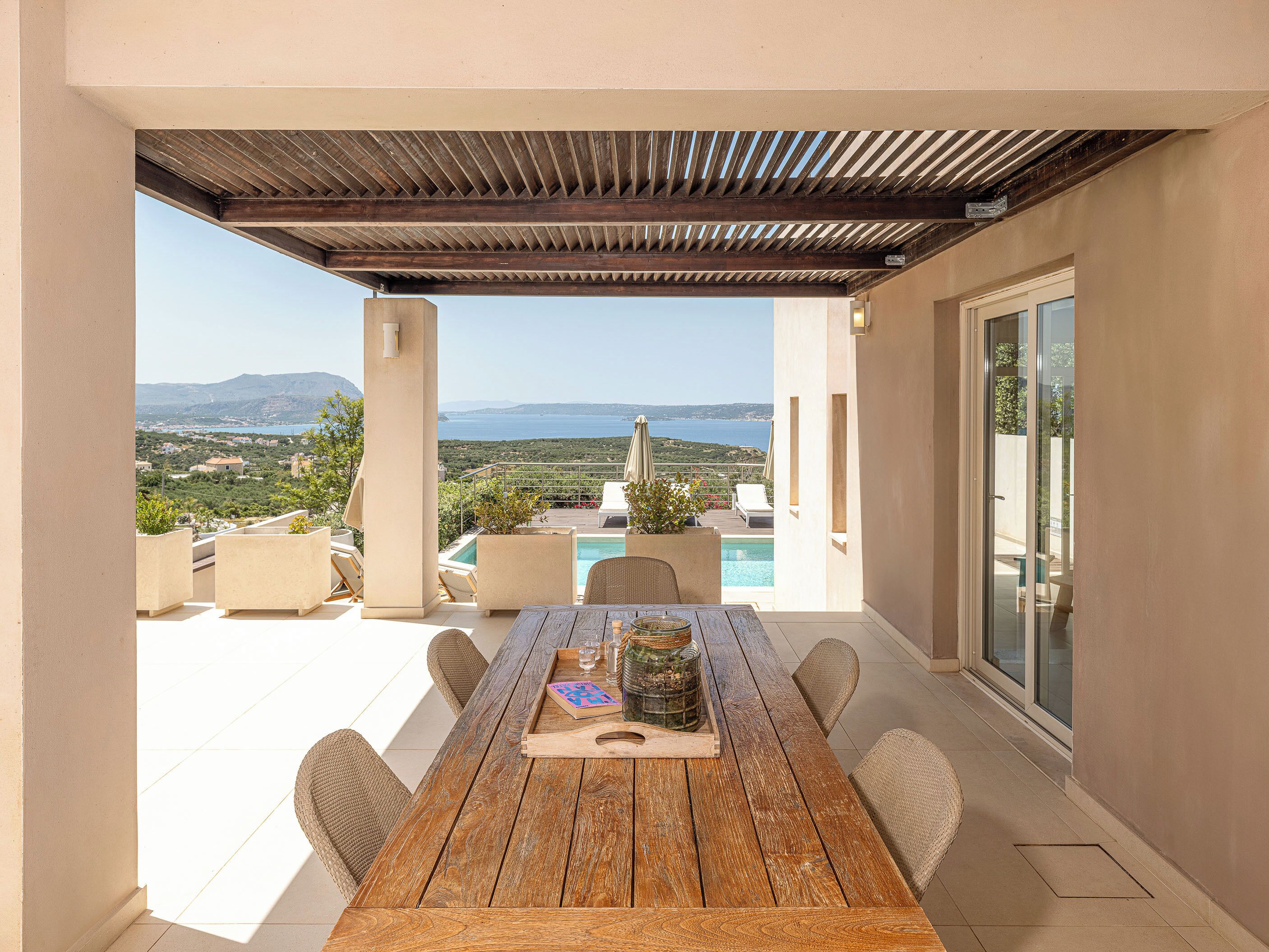 Ein Holztisch mit Stühlen, ein Pool und Blick auf das Meer.