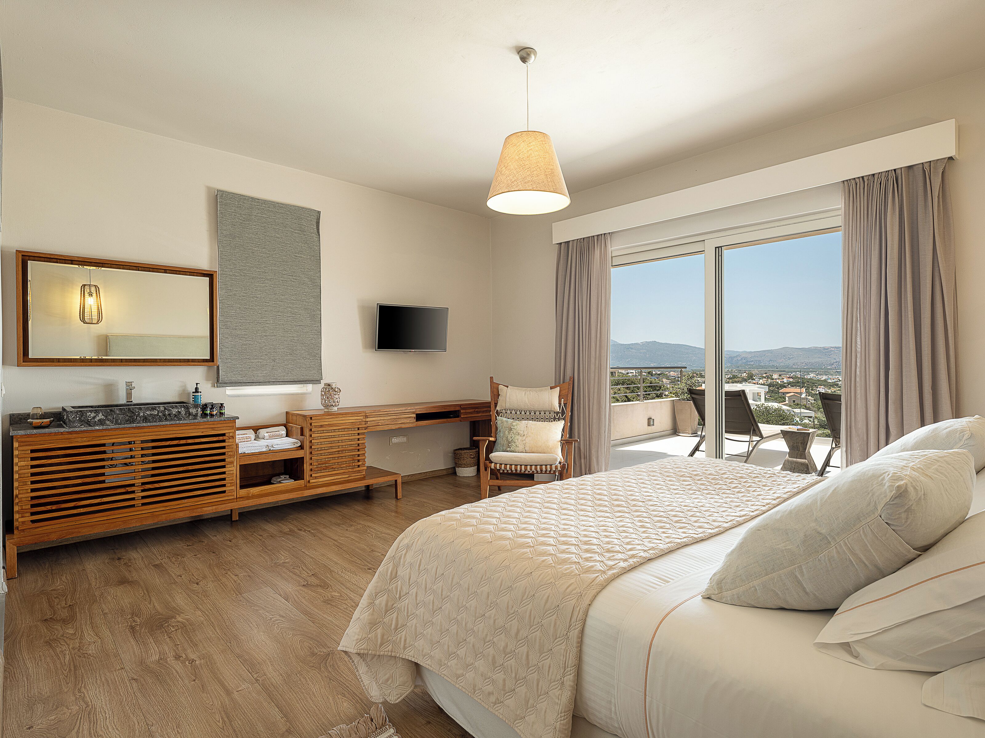 A modern hotel room with a large bed, a wooden vanity, a flat-screen TV, and a balcony with a city view.