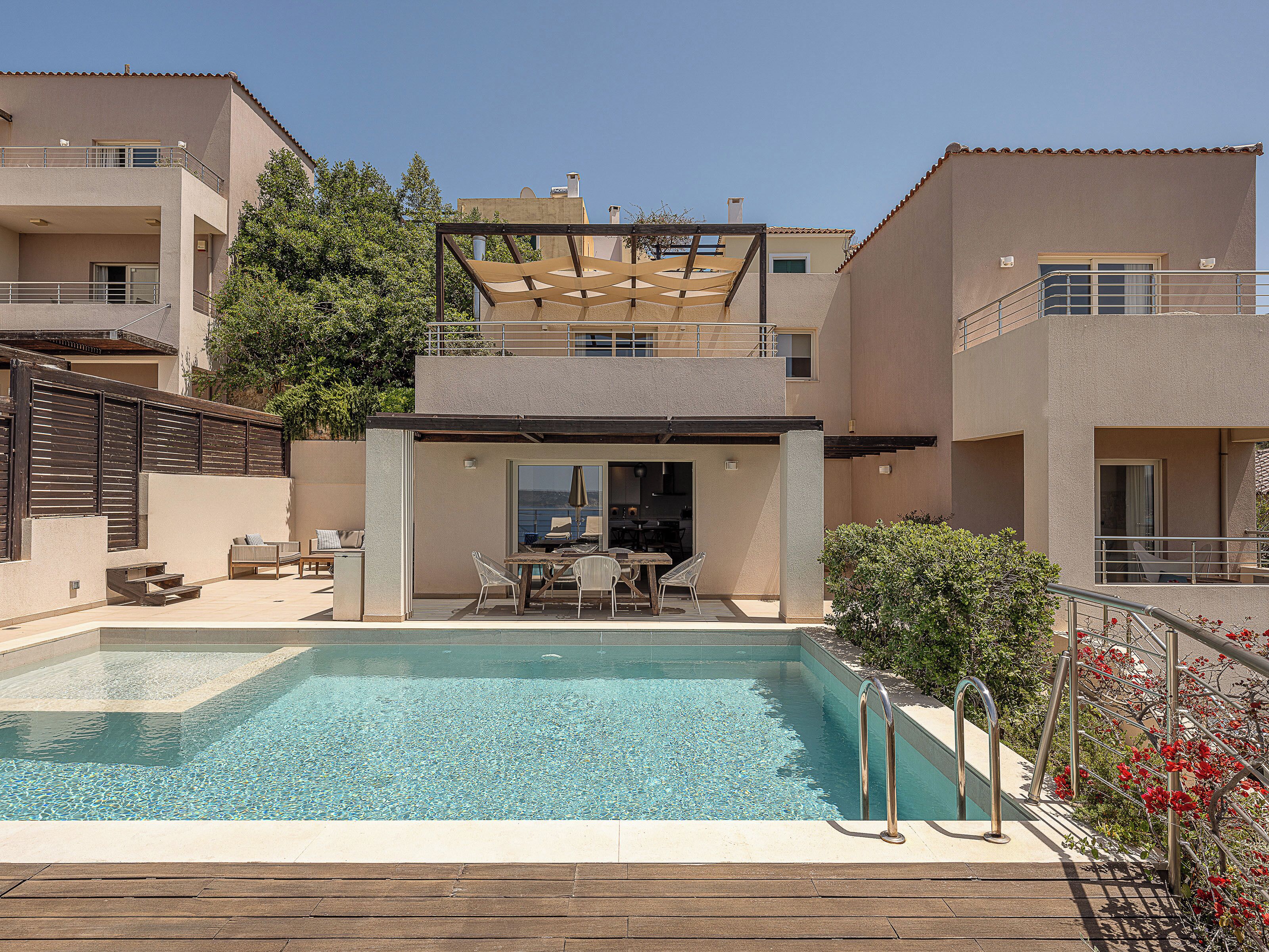 A modern two-story building with a swimming pool, outdoor seating, and a view of the sea.
