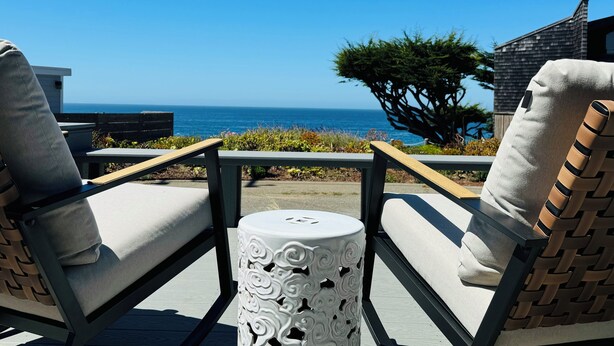 Een terras met twee comfortabele stoelen, een tafeltje en uitzicht op de oceaan.