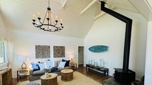 Een ruime woonkamer met een hoge plafond, een zwarte houtkachel, een kroonluchter en een grote decoratie van vissen aan de muur.