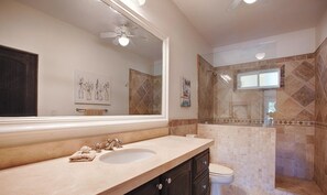 A bathroom with a large mirror, a sink, a toilet, and a shower area.