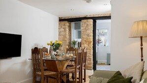 A dining area with a table set for four, surrounded by wooden chairs. A television is mounted on the wall to the left. - The Honey Stone Townhouse, Trendy Townhouse in Chipping Norton (Chipping Norton)