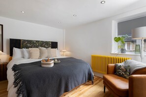 Une chambre moderne avec un lit, des tables de chevet, un radiateur, une fenêtre avec des plantes et une vue sur l’extérieur.