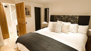 A bedroom with a large bed, wooden flooring, a dark headboard, and a nightstand with a lamp. - The Honey Stone Townhouse, Trendy Townhouse in Chipping Norton (Chipping Norton)