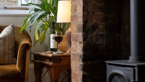 A cozy room with a brick fireplace, a wooden table with a lamp, a potted plant, and a comfortable chair. - The Honey Stone Townhouse, Trendy Townhouse in Chipping Norton (Chipping Norton)
