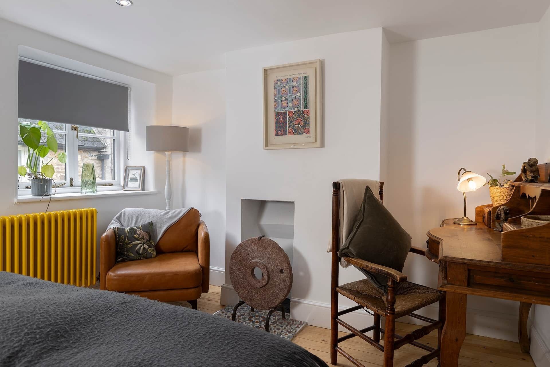 Een gezellige kamer met een leren fauteuil, een rond houten krukje, een klein tafeltje met een lamp en een radiator.