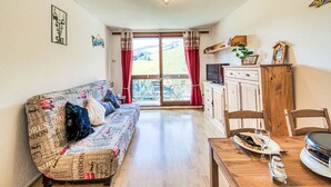 Una sala de estar acogedora con sofá, una mesa de comedor con sillas, televisor y zona de cocina.