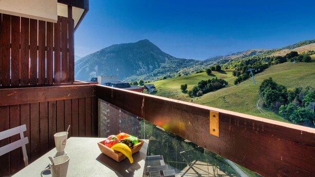 Un balcón con una mesa dispuesta para dos personas, con vistas a un paisaje montañoso.