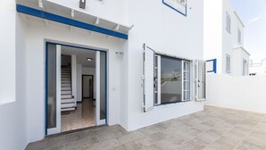 Un bâtiment moderne doté d’un escalier menant à un étage supérieur, d’un espace extérieur couvert avec un sol carrelé et d’une porte à cadre bleu.