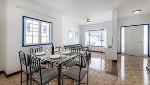 Un vaste espace dédié à la salle à manger, avec une table à plateau en verre, des chaises en métal noir et une vue sur l’extérieur.