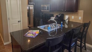 A kitchen with dark wooden cabinets, a stainless steel sink, and two pendant lights. - Majestic Cove | 2BR Branson Condo w/ Table Rock Lake Views (MJ126) (Branson)