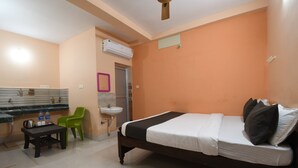 A bedroom with a bed, a small table with bottles, a chair, a sink, and an air conditioner. - RADHA KRISHNA NIWAS (Puri)