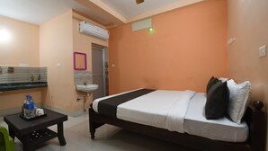 A bedroom with a bed, bedside table, and a bathroom with a sink and mirror. - RADHA KRISHNA NIWAS (Puri)