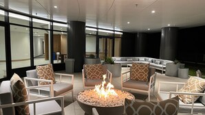 Een moderne lounge met een ronde vuurplaats, comfortabele zithoek en grote ramen met uitzicht op het interieur.