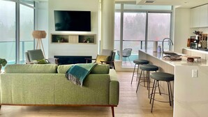 Een moderne woonkamer met een groene bank, een flatscreen televisie en een open haard. Grote ramen bieden uitzicht op het omliggende landschap.