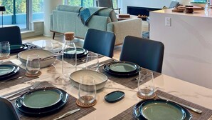 Een moderne eetruimte met een grote tafel gedekt voor vier personen, een bank en een aan de muur bevestigde televisie.