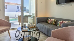 A modern living room with a grey sofa, a round coffee table, and a glass door leading to an outdoor area with a pool and furniture. - Victoria by Interhome (Budoni)