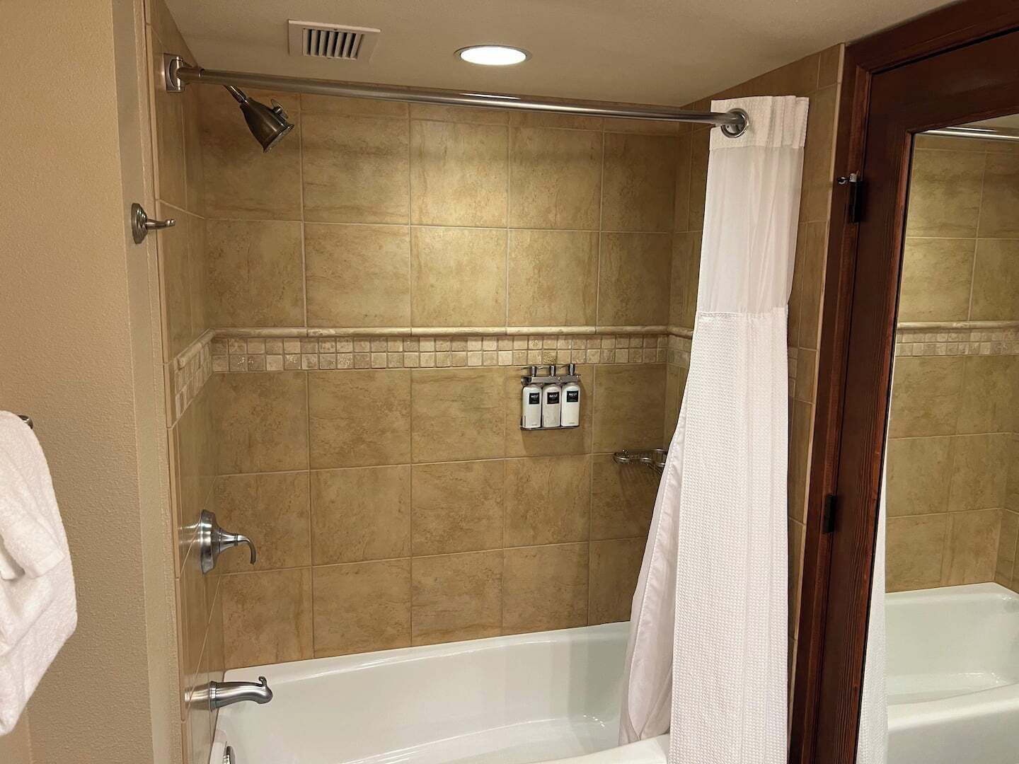 A bathroom with a bathtub, a shower curtain, and a towel rack with bottles.