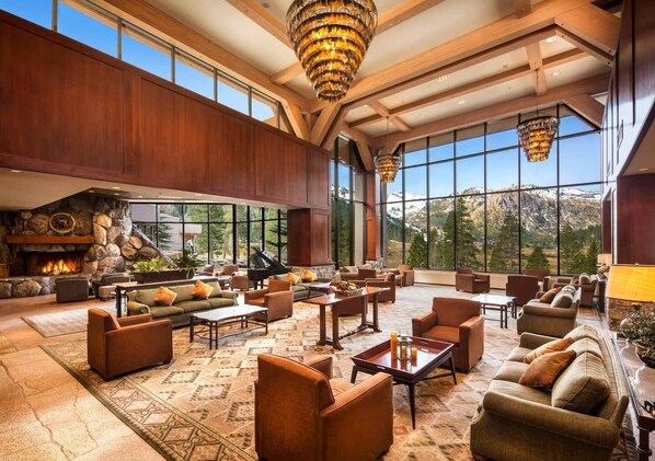 Un hall d’entrée spacieux avec une cheminée en pierre, plusieurs coins salon et de grandes fenêtres offrant une vue sur les montagnes.