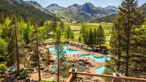 Un resort con varias piscinas rodeadas de árboles, un campo de golf y montañas al fondo.