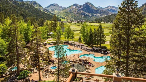Un complexe hôtelier doté de plusieurs piscines entourées d’arbres, d’un parcours de golf et offrant une vue sur les montagnes en arrière-plan.