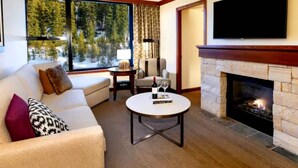 Una sala de estar moderna con chimenea, un televisor grande y vistas a un bosque por la ventana.