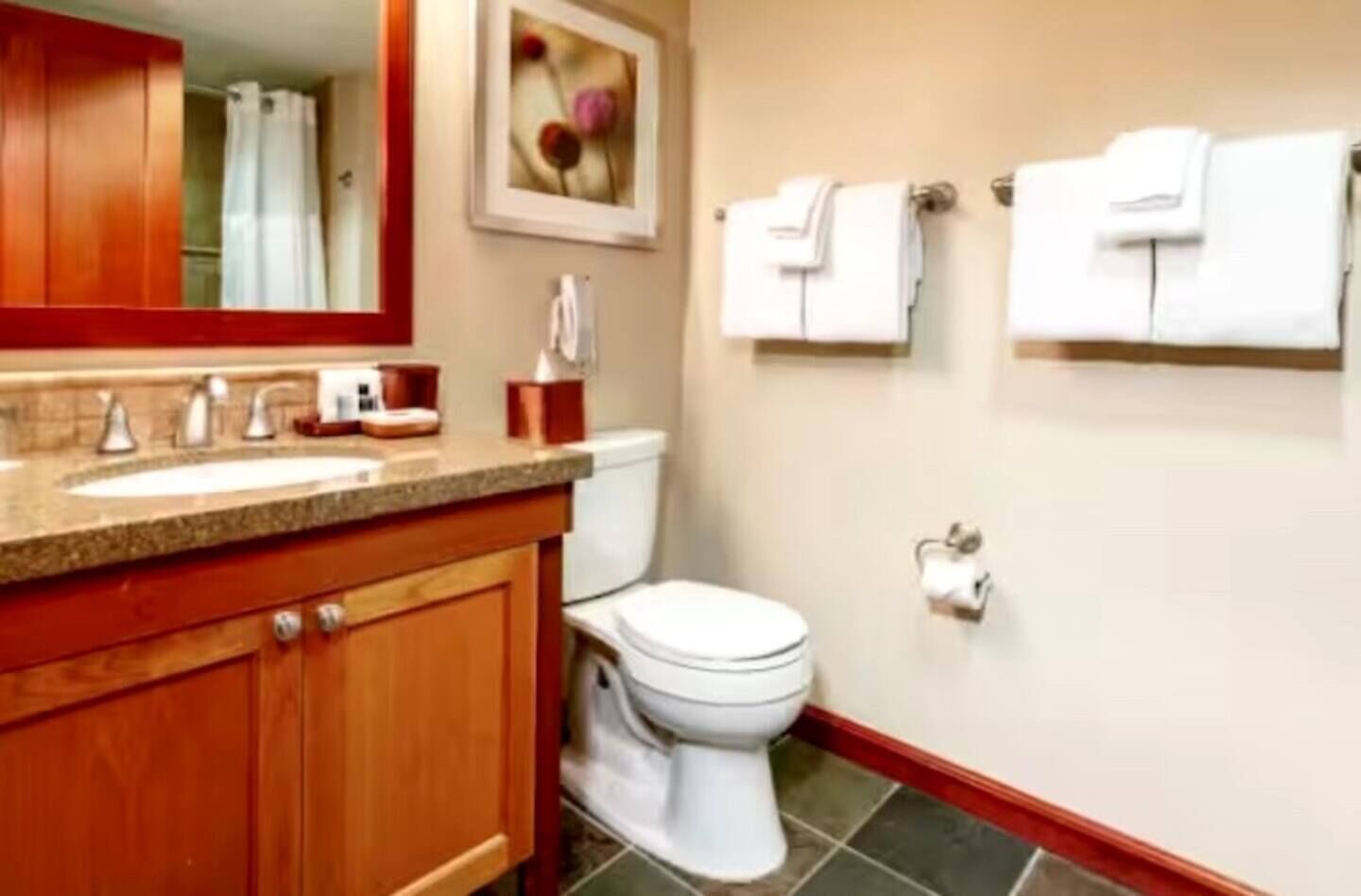 A bathroom with a wooden vanity, a sink, a toilet, and two towel racks.